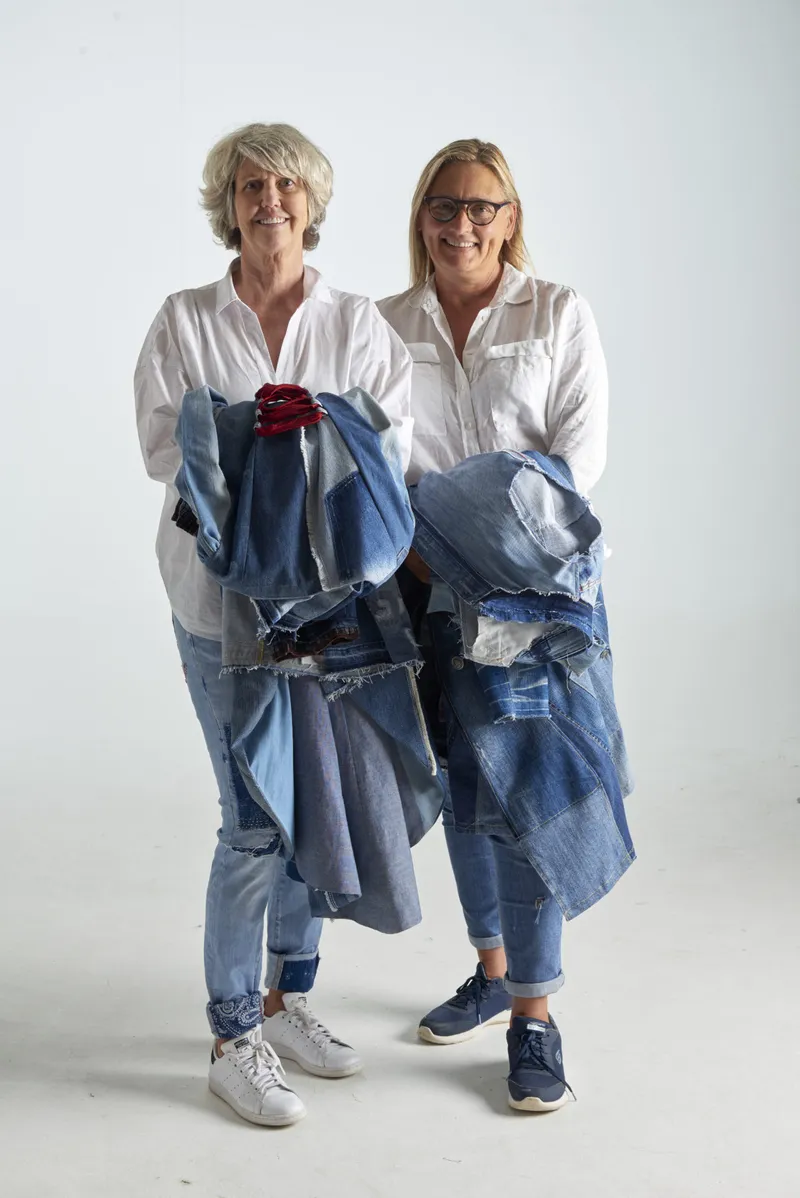 anne and cheryl, each holding armfuls of denim pieces mid-sort