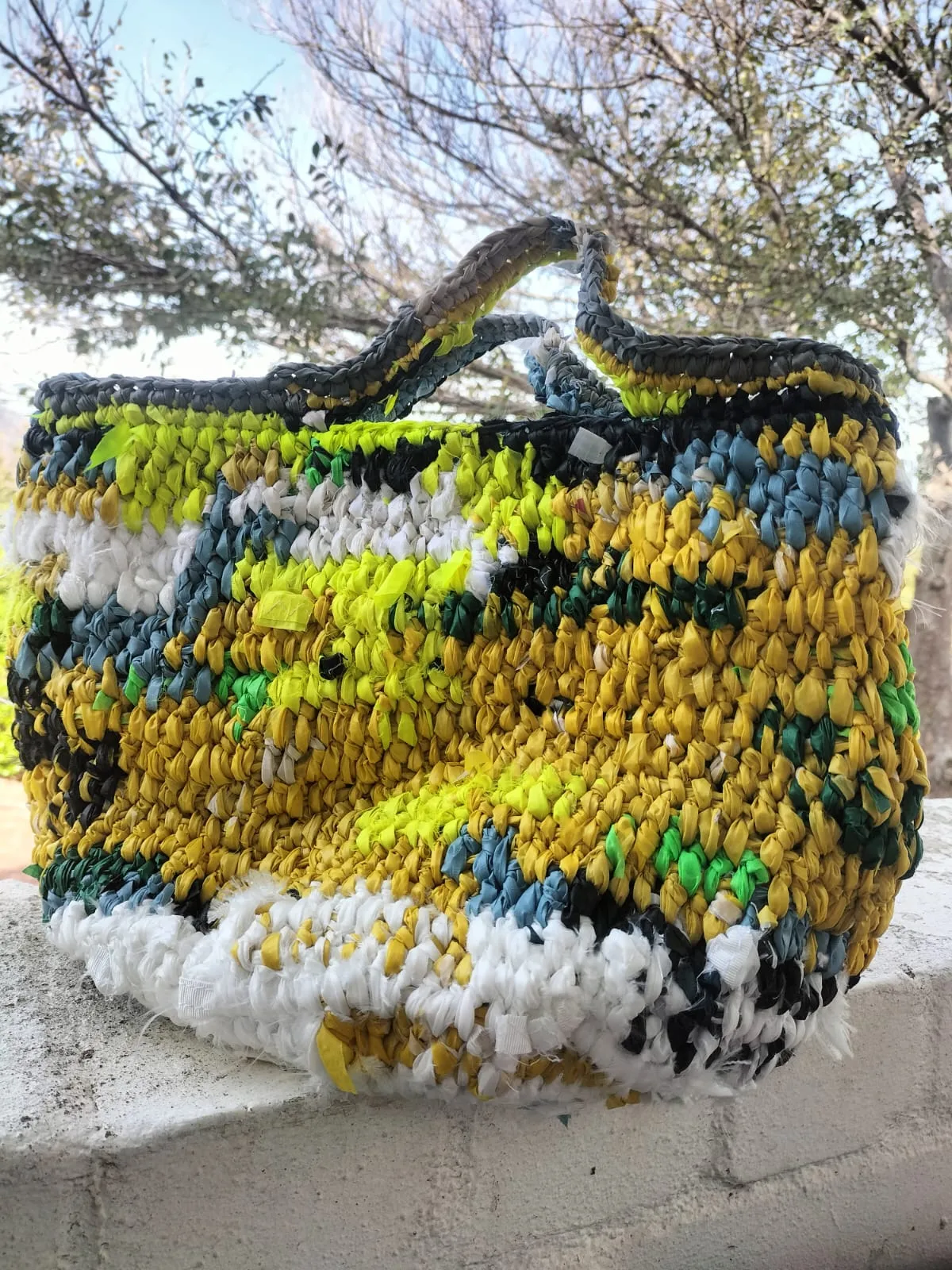 crocheted tote made from strips of recycled plastic — yellow, green, blue and white