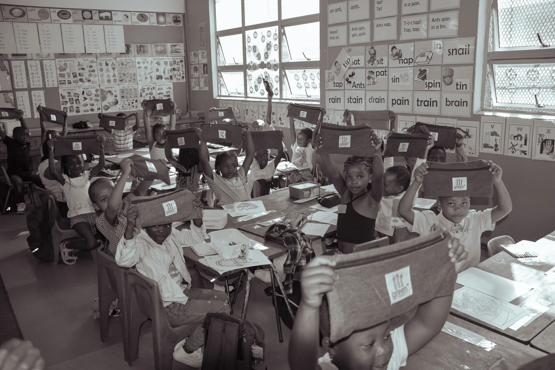 children in a classroom holding up green° denim pencil cases