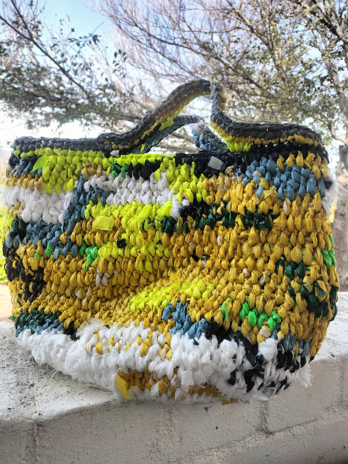 crocheted tote made from strips of recycled plastic — yellow, green, blue and white
