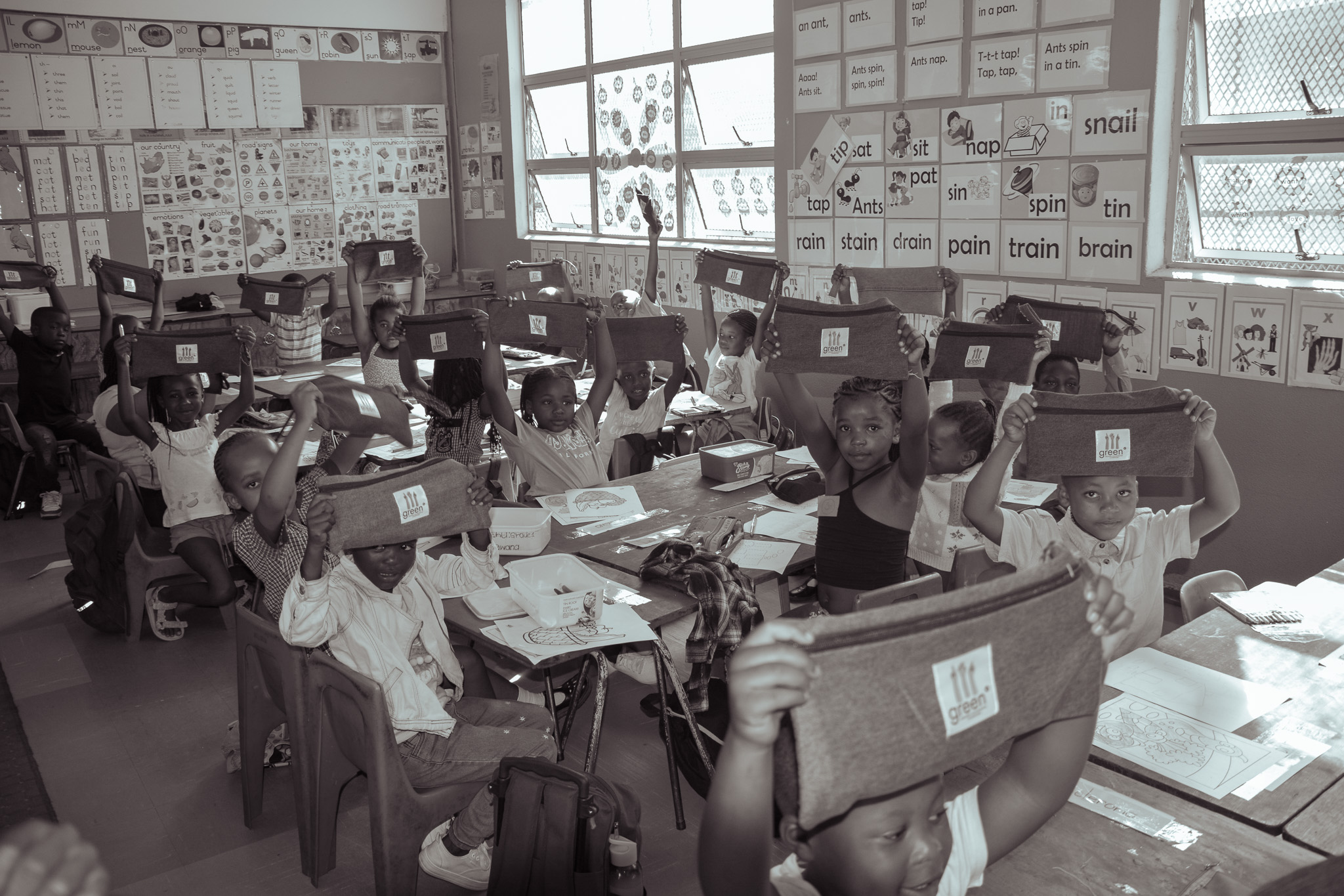 children in a classroom holding up green° denim pencil cases